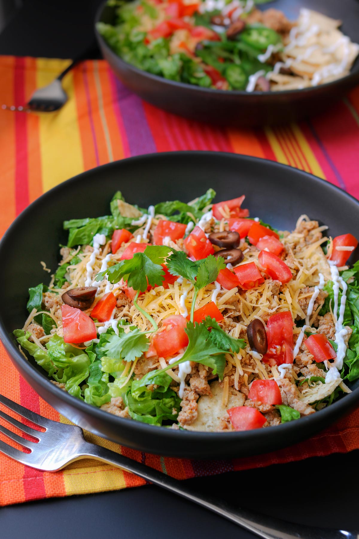 two plates of taco salad on colorful mat with forks.