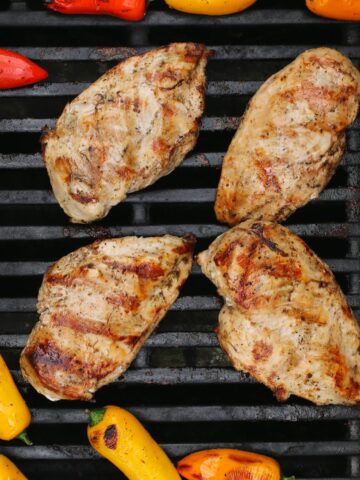 four chicken breasts on the grill surrounded by mini bell peppers.