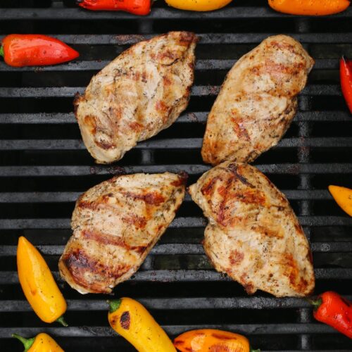 four chicken breasts on the grill surrounded by mini bell peppers.