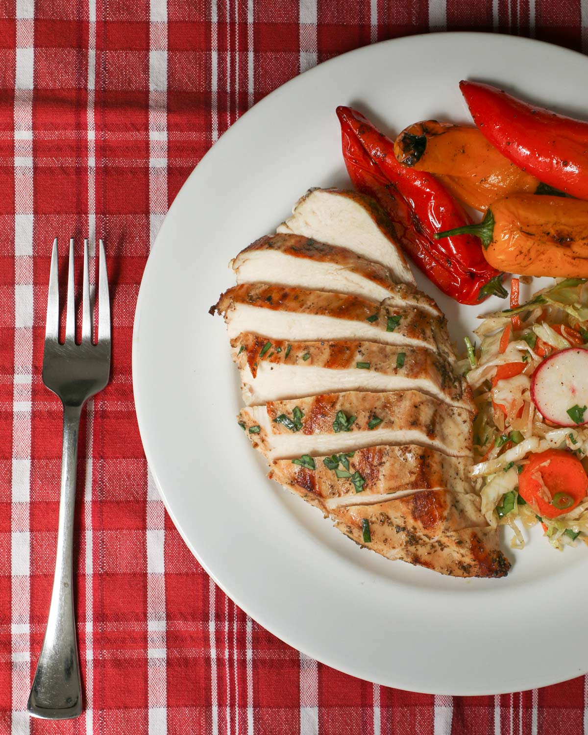 sliced grilled chicken breast fanned on plate with peppers and coleslaw.