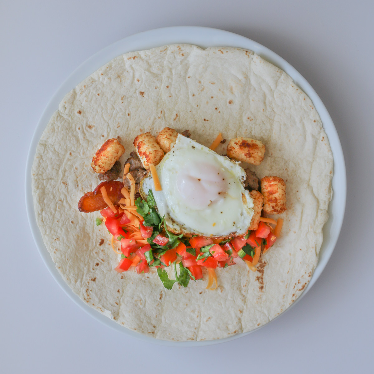 tortilla laid out with fillings for breakfast burrito.