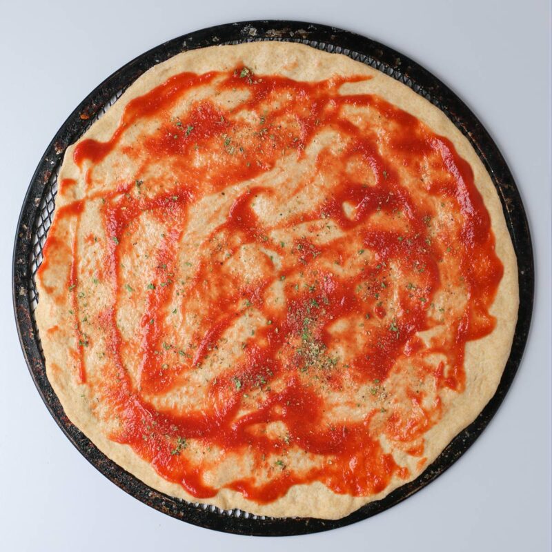 pizza crust spread with tomato sauce and sprinkled with spice blend.