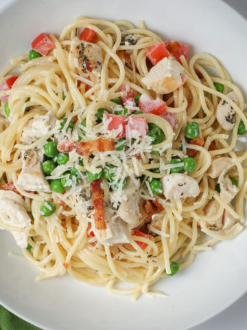 overhead shot of a white bowl filled with chicken pasta with peas and tomatoes.