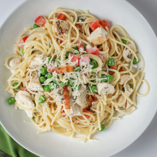 overhead shot of a white bowl filled with chicken pasta with peas and tomatoes.