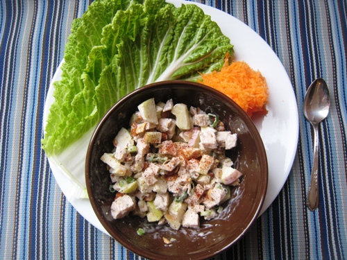 A bowl of chicken salad on a plate with cabbage leaves