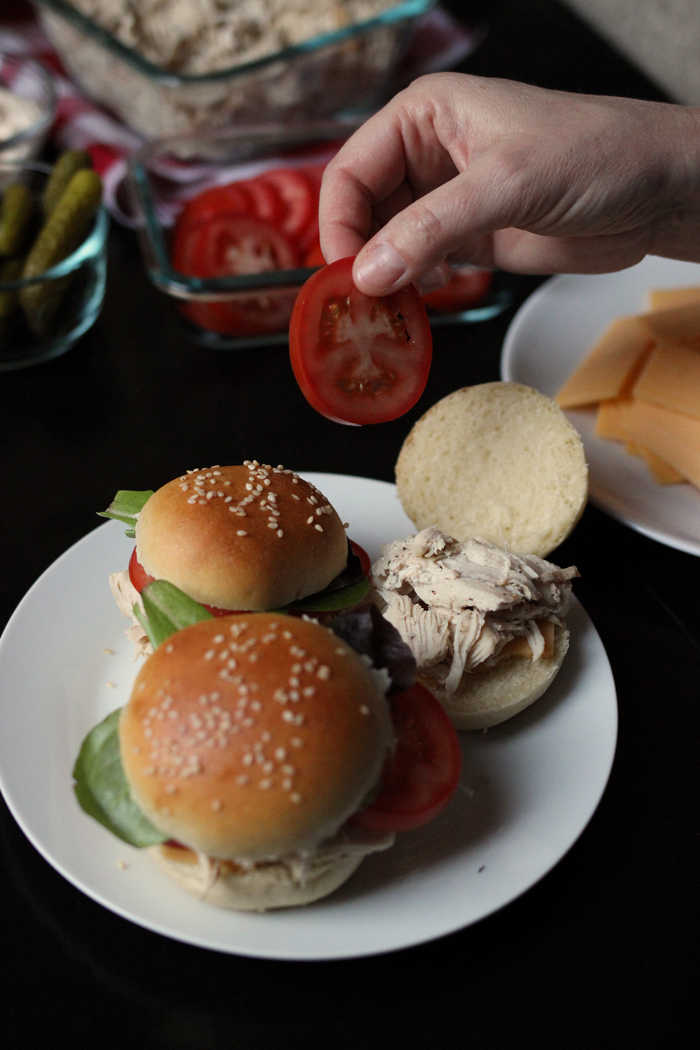 A person assembling pulled chicken sliders
