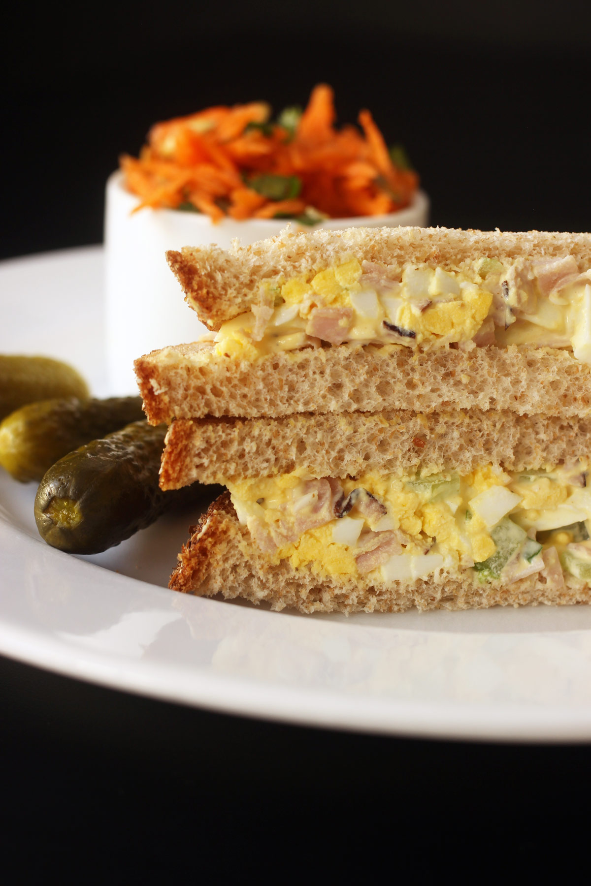 stacked halves of egg salad sandwich on plate with pickle