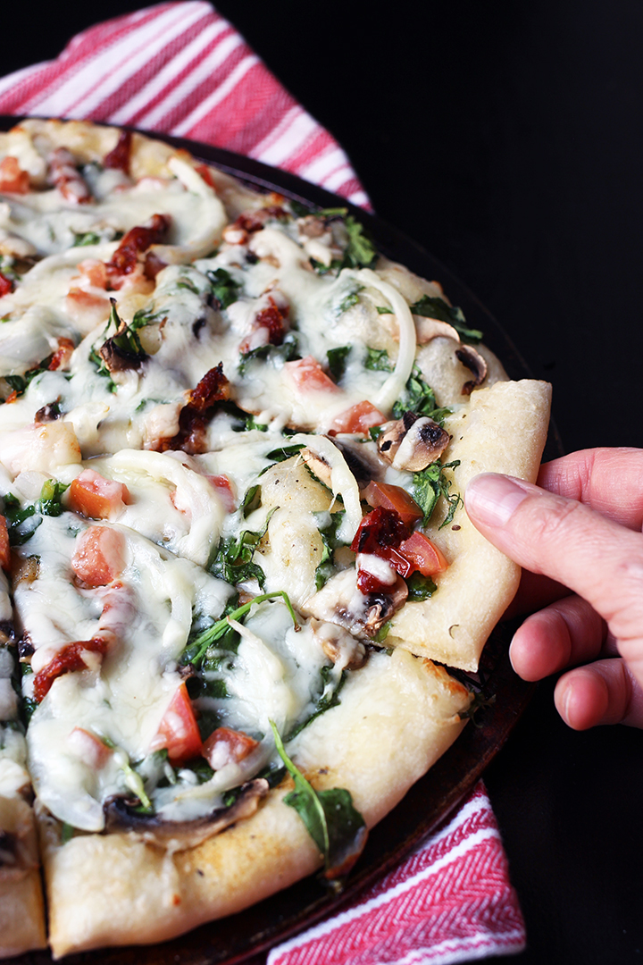 hand pulling slice of meatless kale pizza off pan