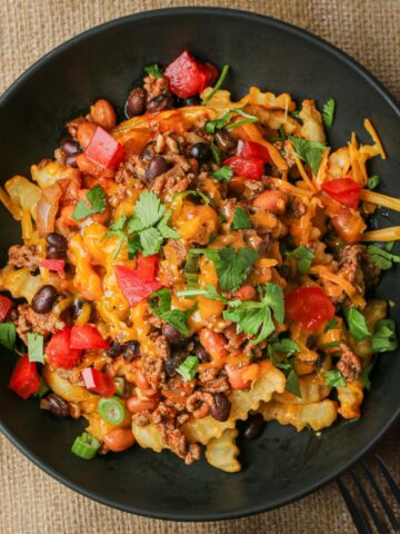 black bowl of Chili Cheese Fries with lots of toppings.