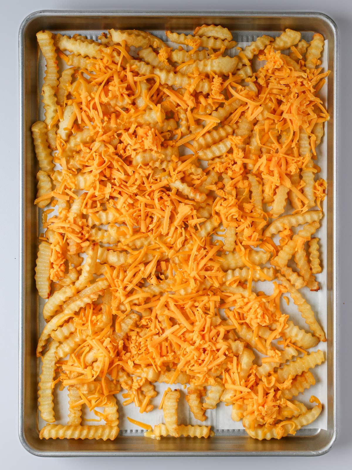 cheese sprinkled on fries in baking sheet.