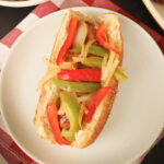 hot dog in whole wheat bun topped with sauteed peppers and onions.