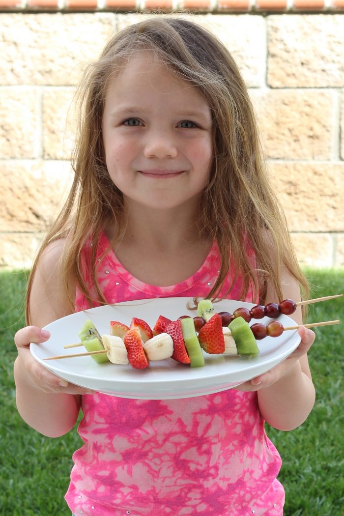 girl holding platter of fruit kabobs