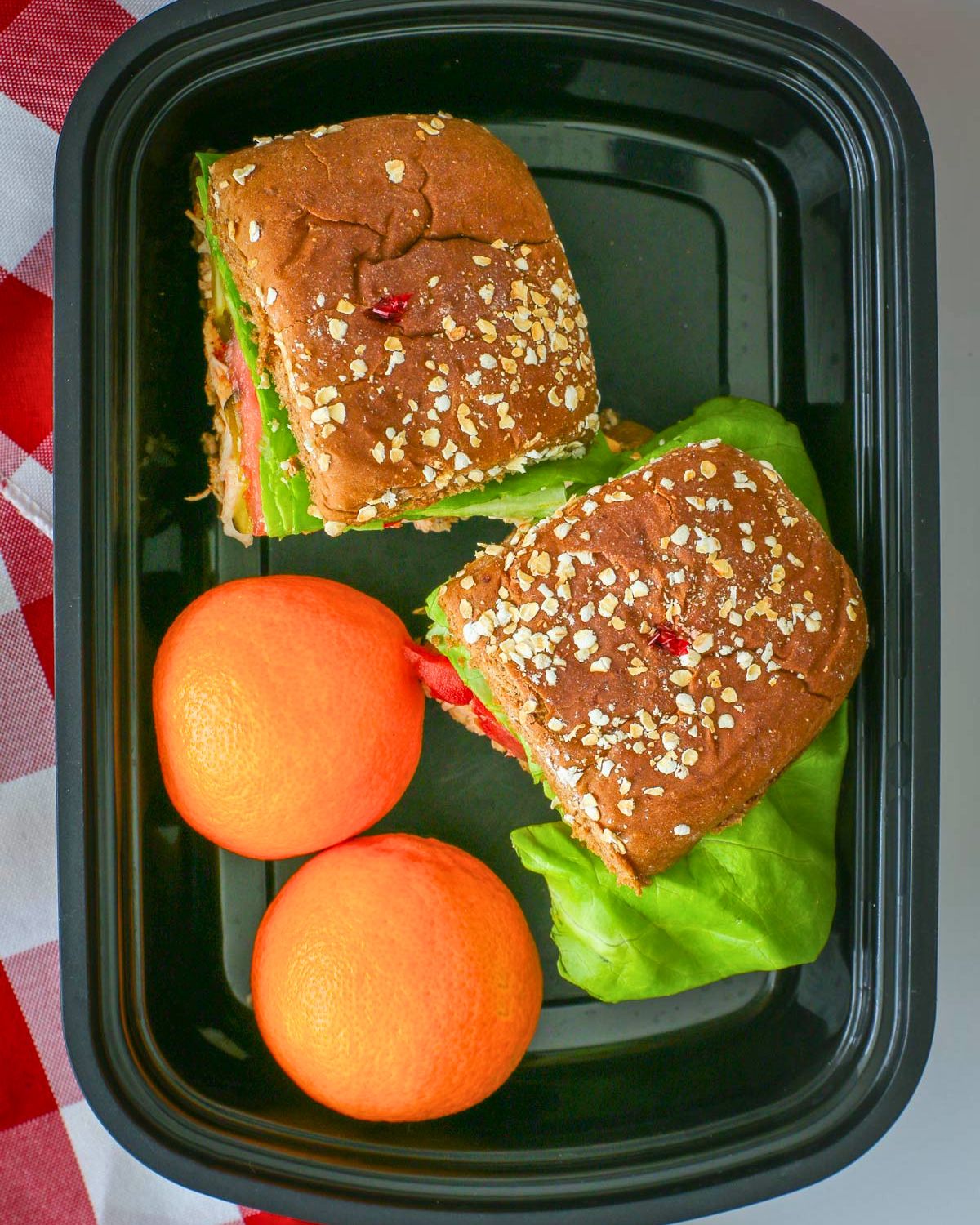 chicken sliders and two cuties in a meal prep box next to a checked cloth.