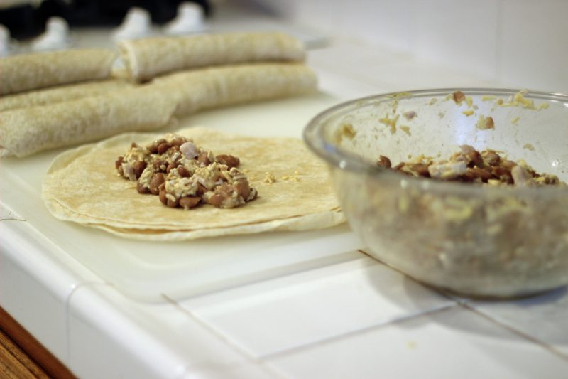 A bowl of burrito filling next to a stack of tortillas