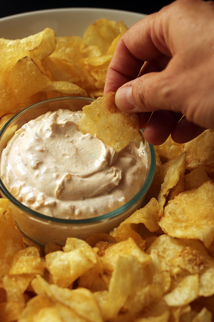 Hand dippt Kartoffelchips in Zwiebel-Dip