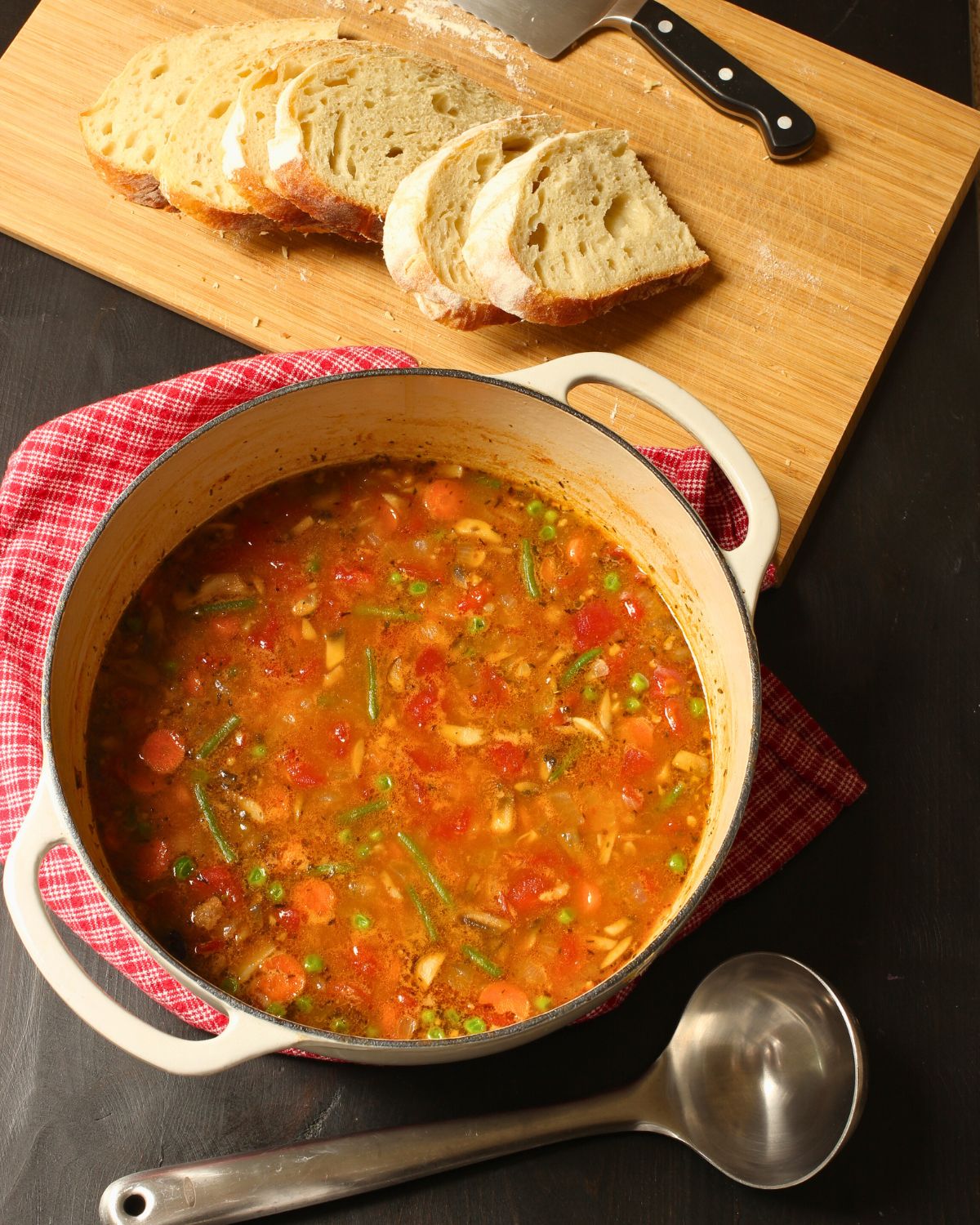 pot of stone soup with a cutting board of bread and a knife.
