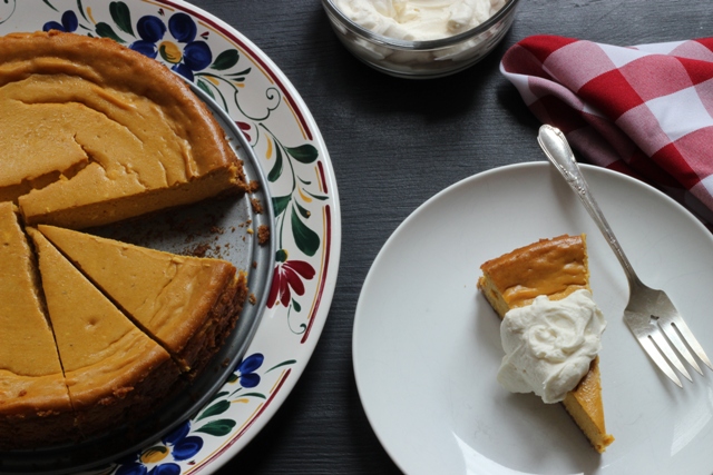 Pumpkin Spice Cheesecake with a slice cut out on a plate with whipped cream.