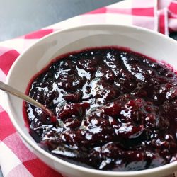 spoon dipped in bowl of cranberry sauce atop red checked cloth