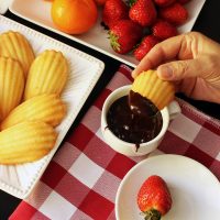 hand dipping madeleine into chocolate fondue next to plates of dippers
