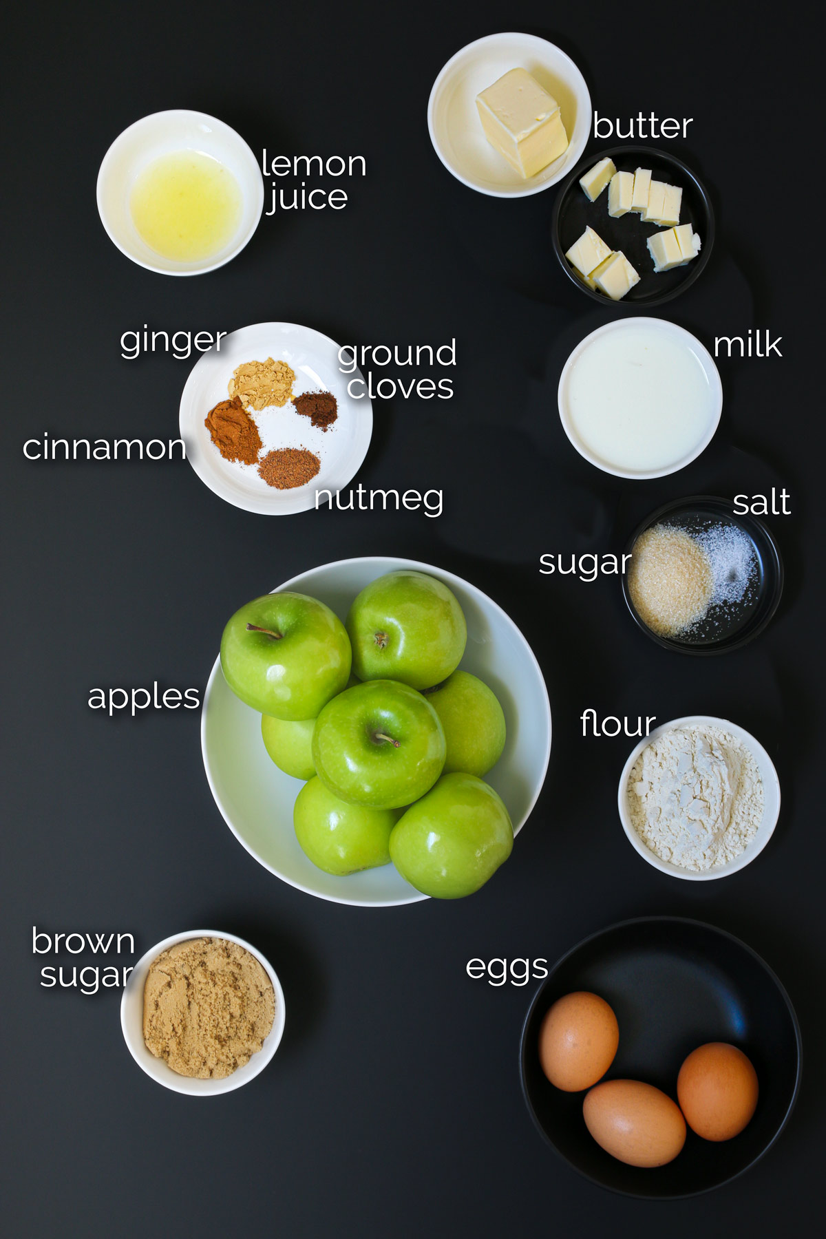 ingredients for puffed pancake with apples laid out on a black table top.