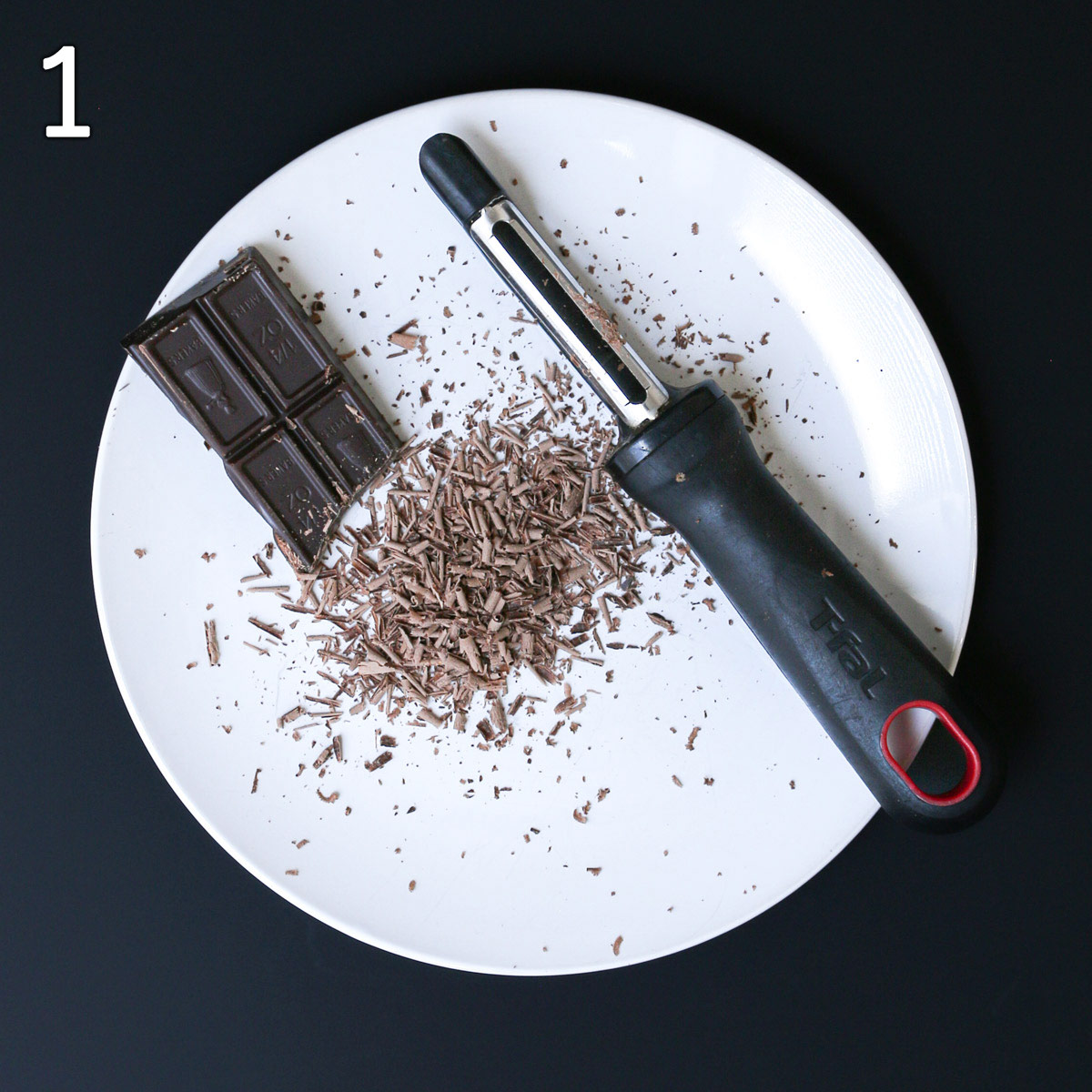 chocolate shavings on a plate with vegetable peeler and square of baking chocolate.