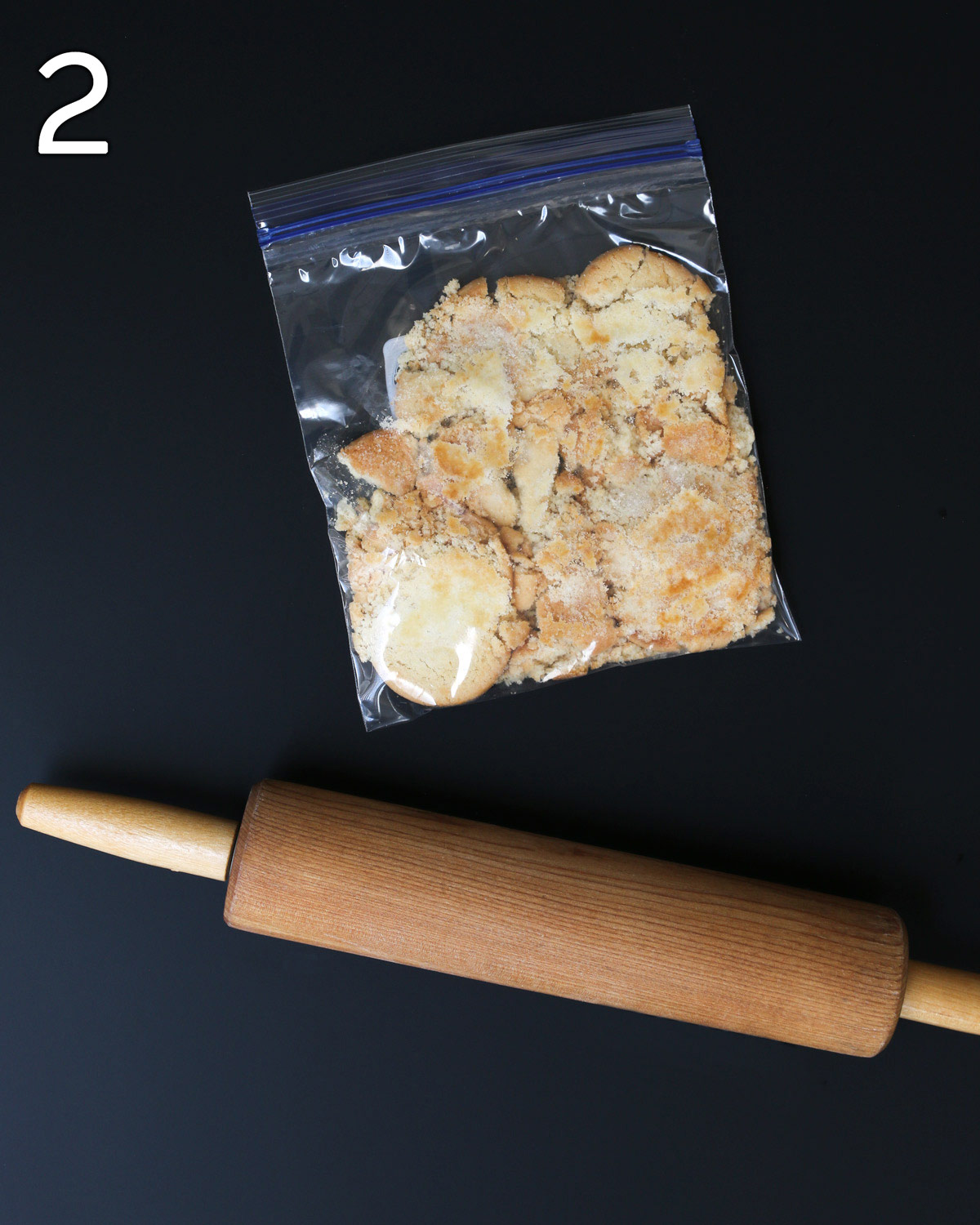 cookies in bag crushed with rolling pin on black table.