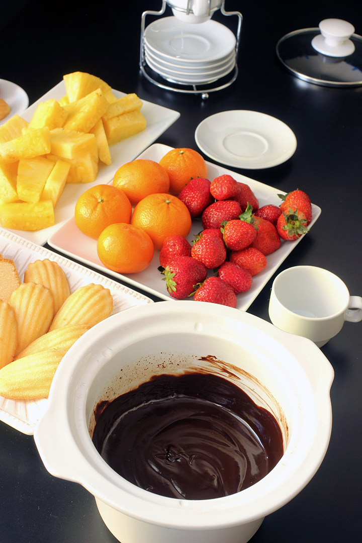 slow cooker crock full of chocolate fondue with plates of fruit and cake