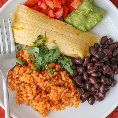 close up overhead shot of cheese tamale on plate with rice, beans, and condiments.