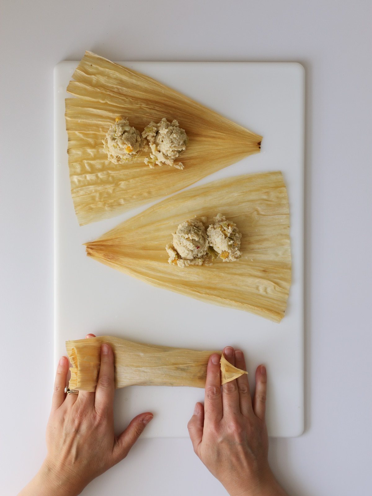 folding in the sides of the bottom tamale on the work surface.