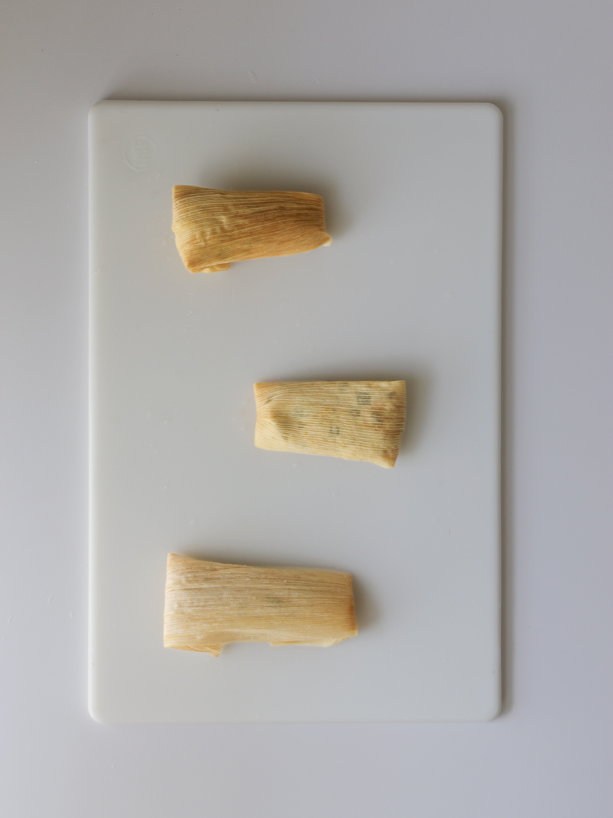 three rolled tamales on the work surface.