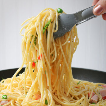 square crop of scooping pasta with tongs from black bowl.