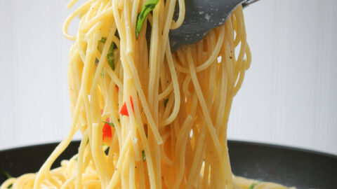 square crop of scooping pasta with tongs from black bowl.