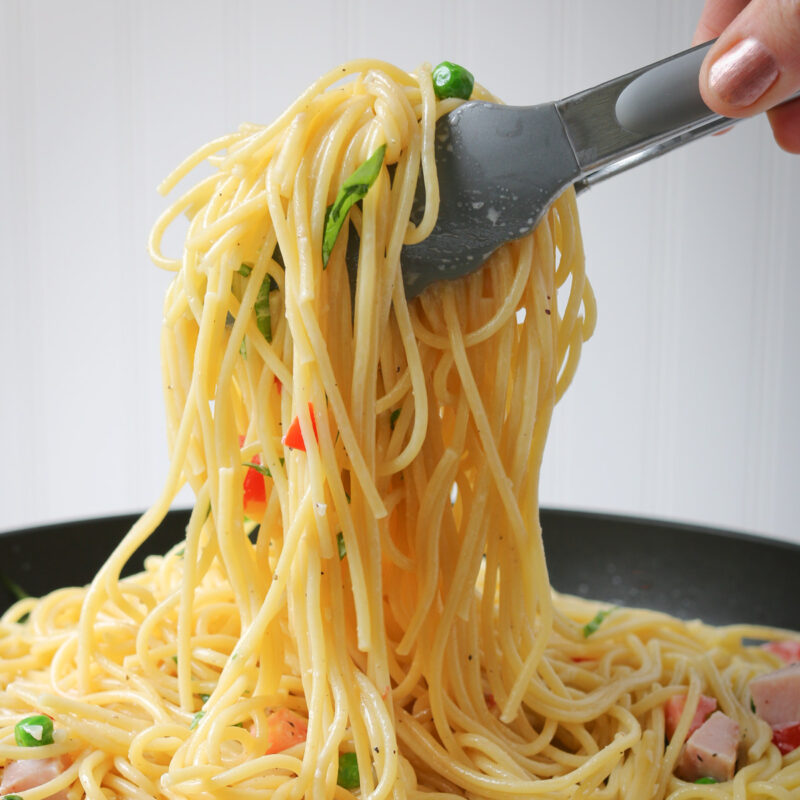 square crop of scooping pasta with tongs from black bowl.