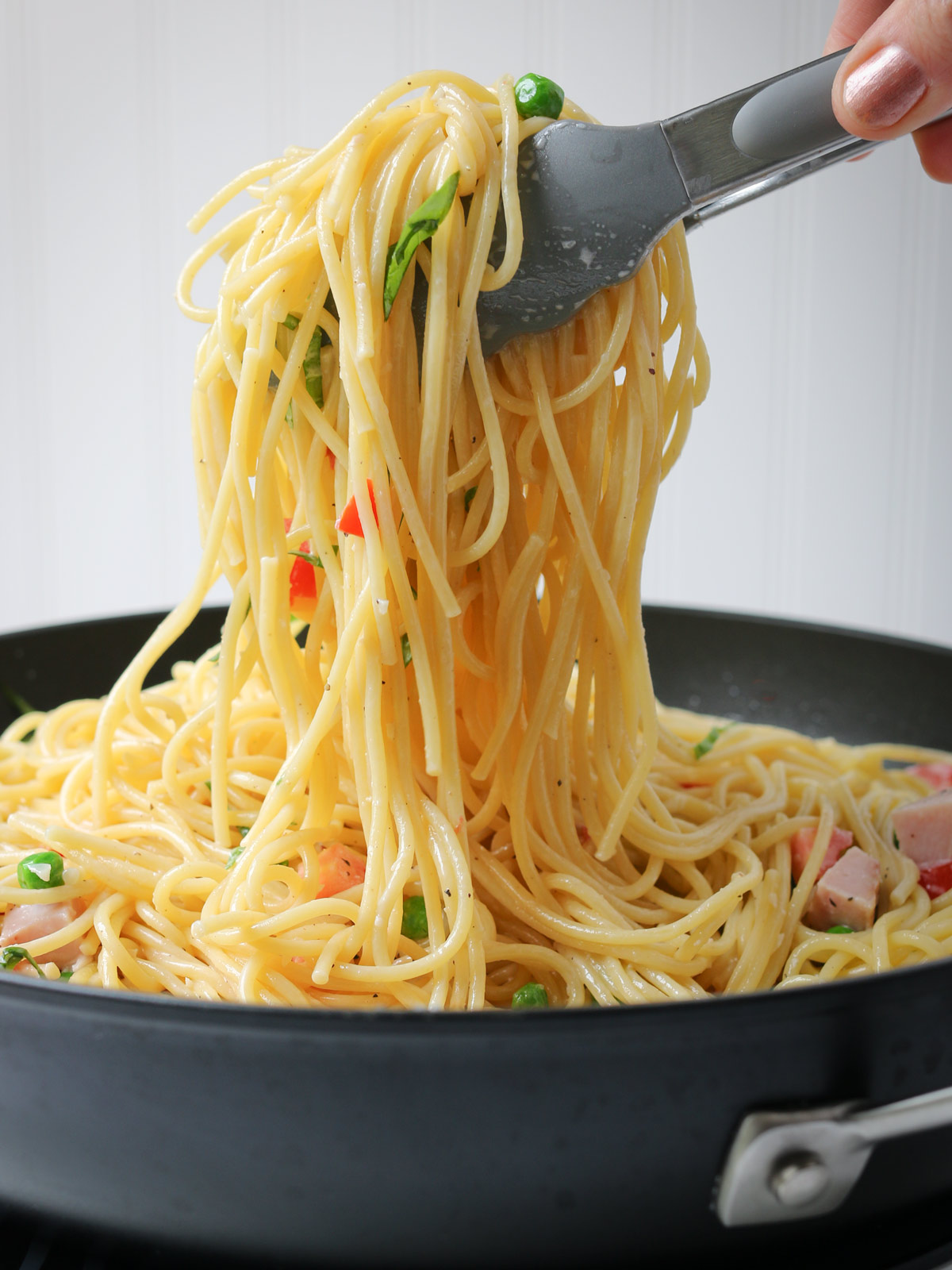 scooping pasta up with tongs from a black bowl.