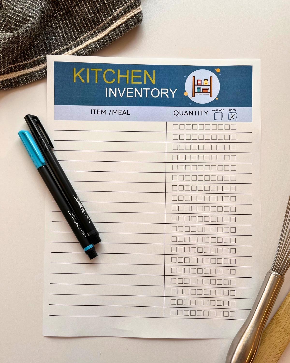 kitchen inventory worksheet on table with kitchen towel, pens, and utensils.