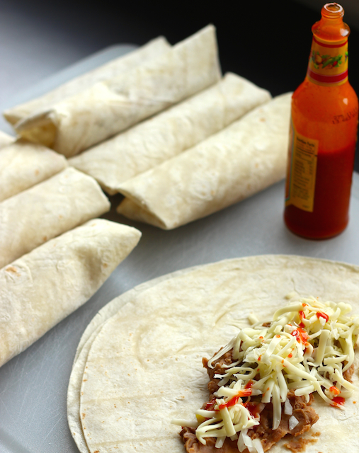 stack of burritos on board with one being assembled