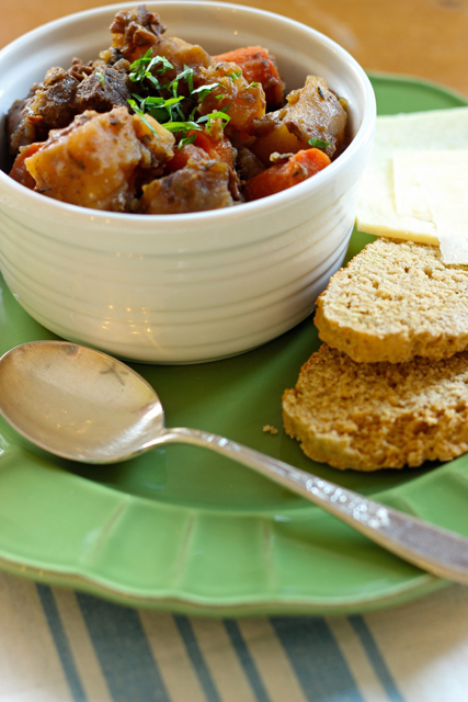 A bowl of stew on a plate, with bread and cheese