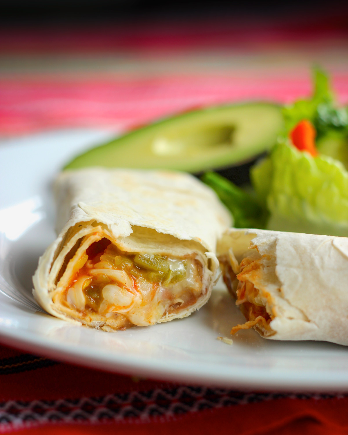 dinner plate with cut bean burrito and half avocado.