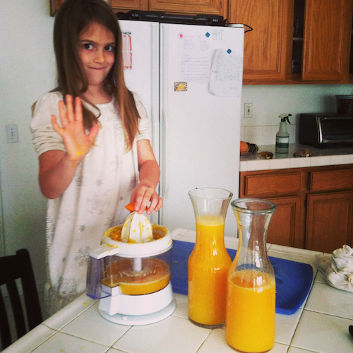 girl standing in a kitchen juicing oranges