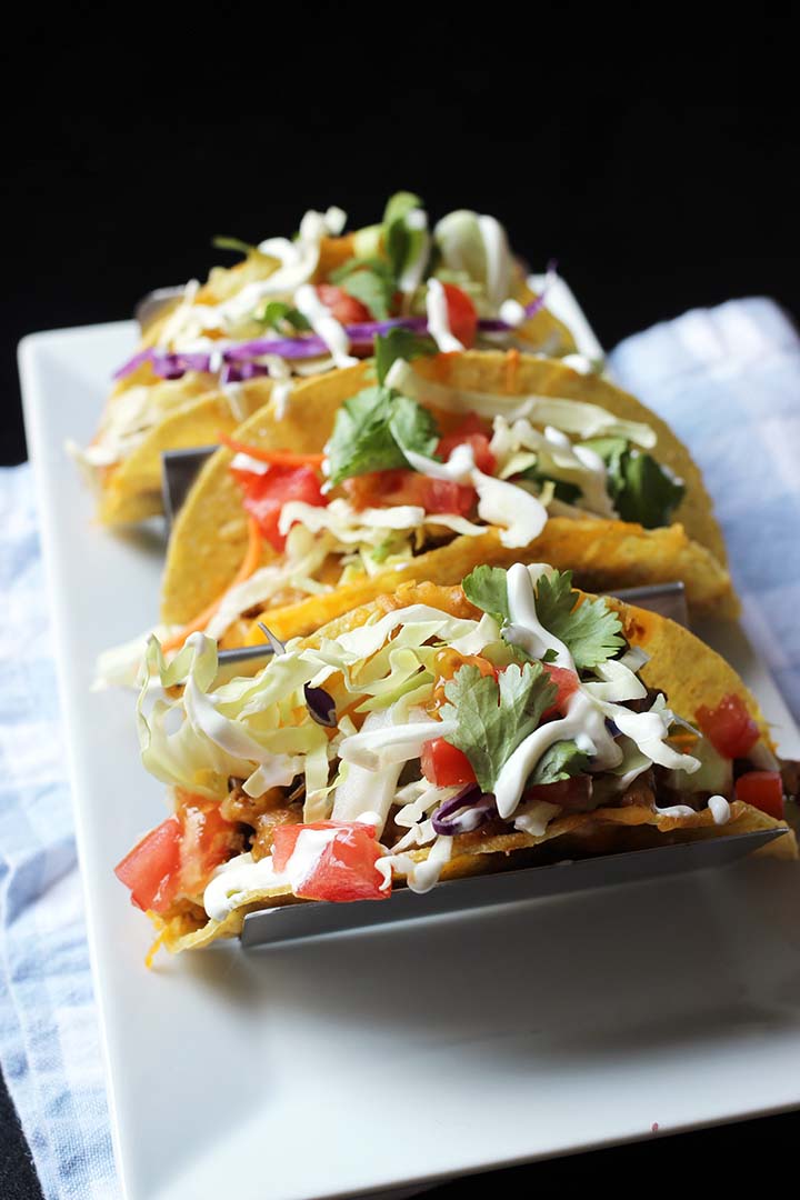 tacos in taco tray on white plate with blue checked napkin