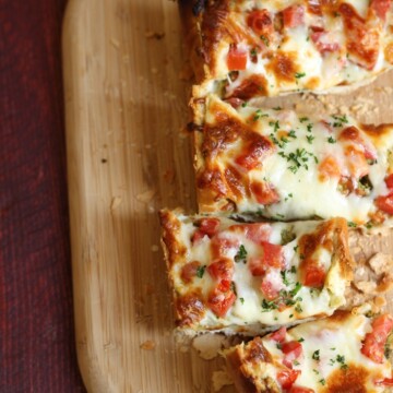 french bread pizza, sliced on a wooden cutting board
