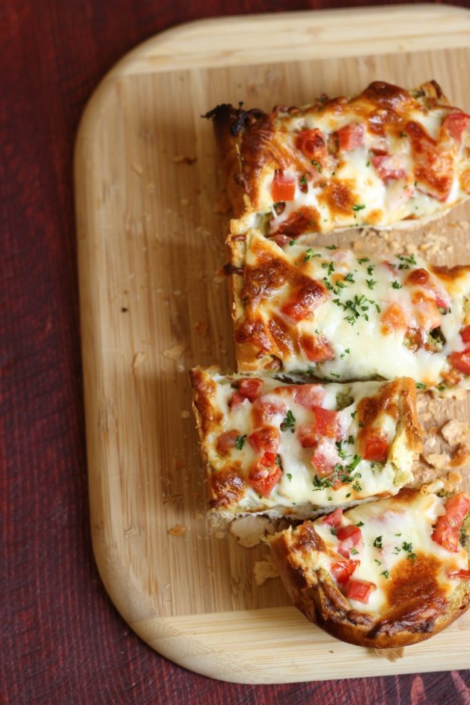 french bread pizza, sliced on a wooden cutting board