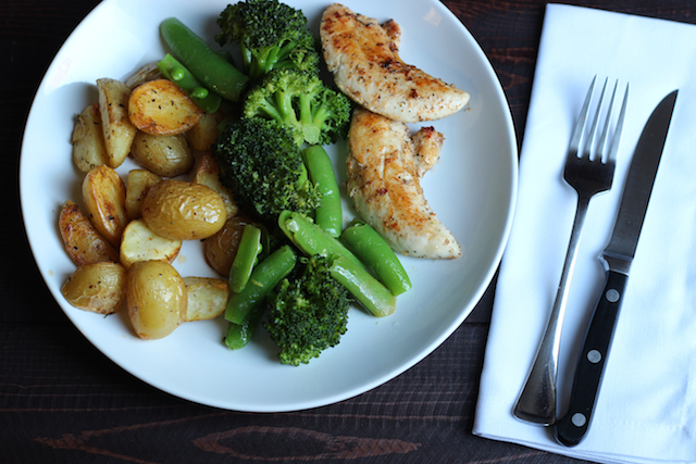 A plate of chicken with broccoli, peas, and potatoes