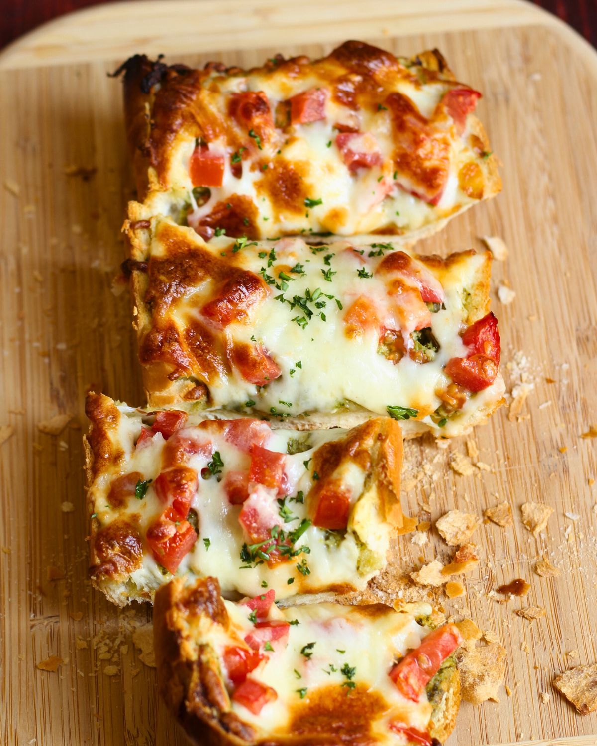 Pesto French bread pizza sliced into strips on a wood cutting board.