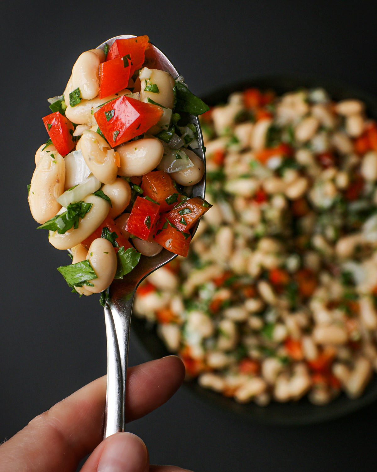 overhead shot of spoonful of white beans salad in focus suspended over a bowl of salad.