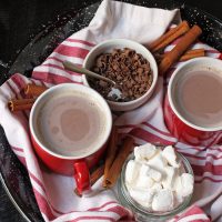 hot cocoa in red mugs on tray with toppings