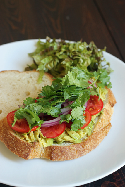een bord met een broodje en een salade, met avocado en koriander