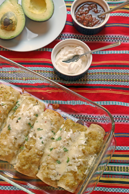 A pan of enchiladas on table, with sour cream