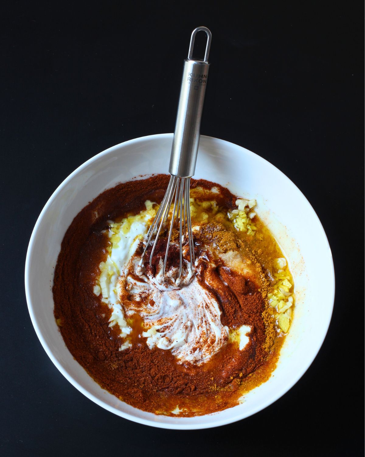 tandoori chicken marinade swirled in a white bowl with a whisk.