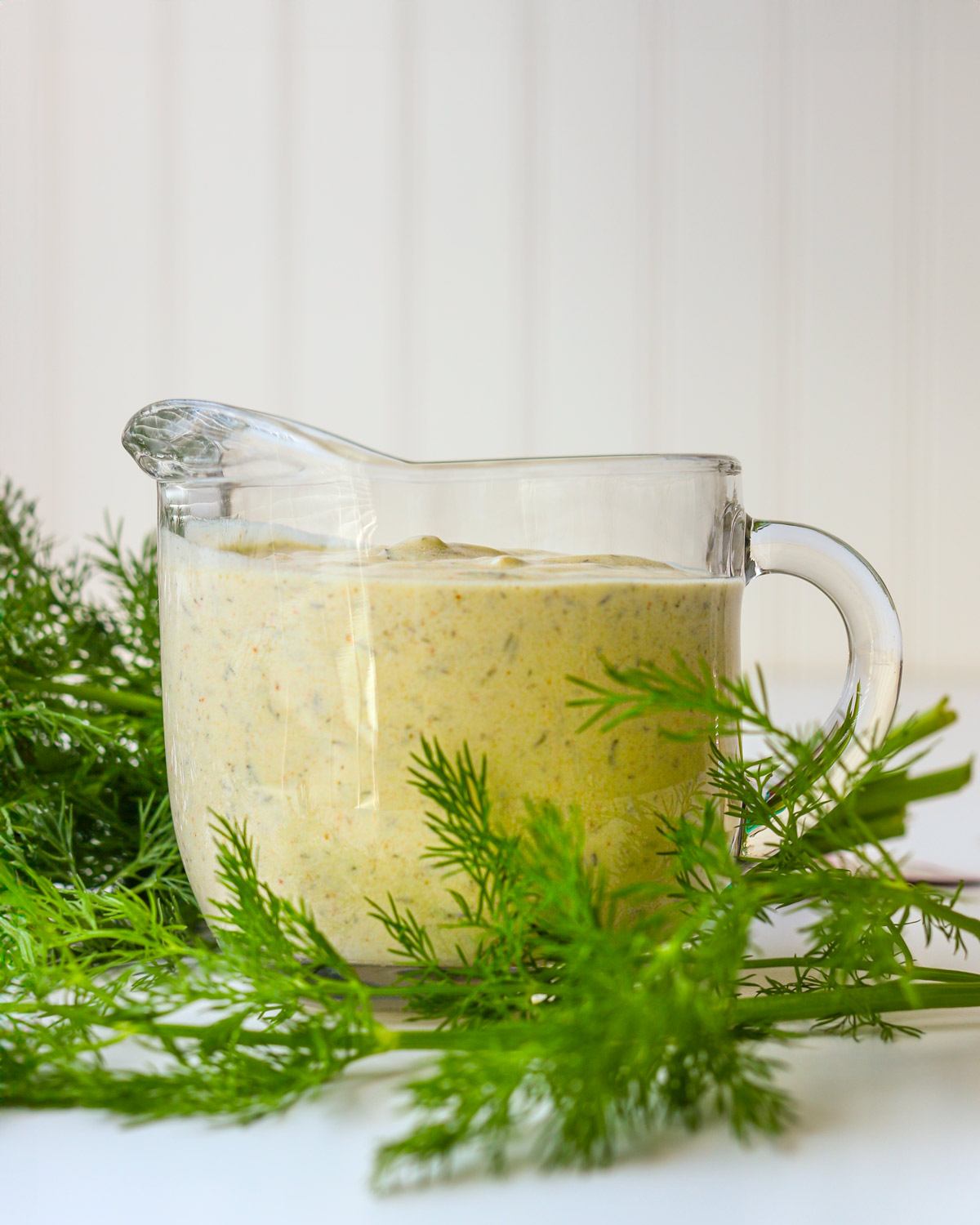 small glass pitcher of yogurt dill dressing with fresh dill sprigs.